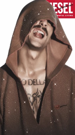 Damiano David wearing a brown hooded sweatshirt with rhinestones against a white background for Diesel Fall 2024 ad campaign.