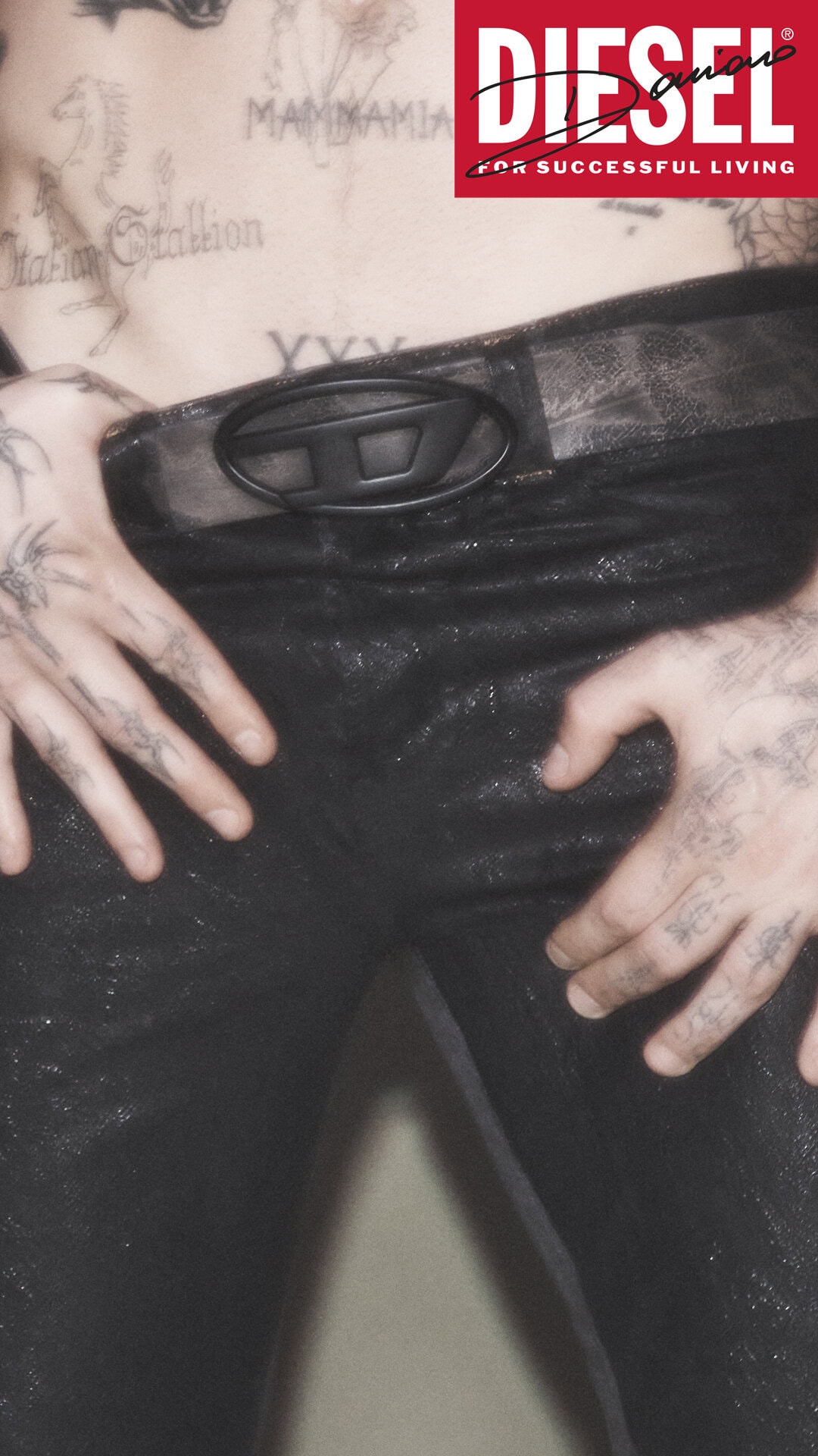 Close-up of Damiano David wearing black denim jeans and a D-logo belt with tattoos visible on torso and hands, for Diesel.
