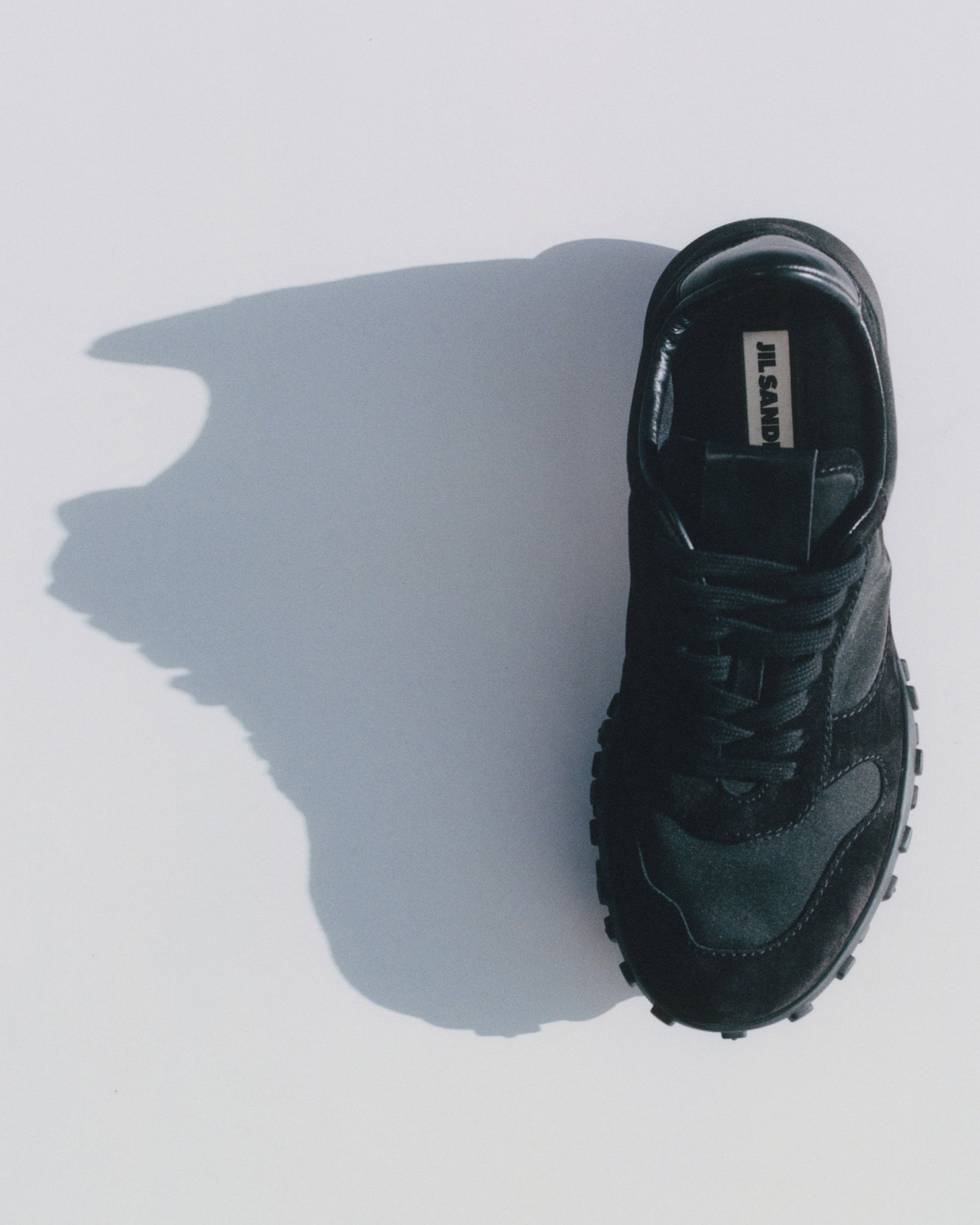 Overhead studio shot of a black sneaker on a light grey background casting a long shadow