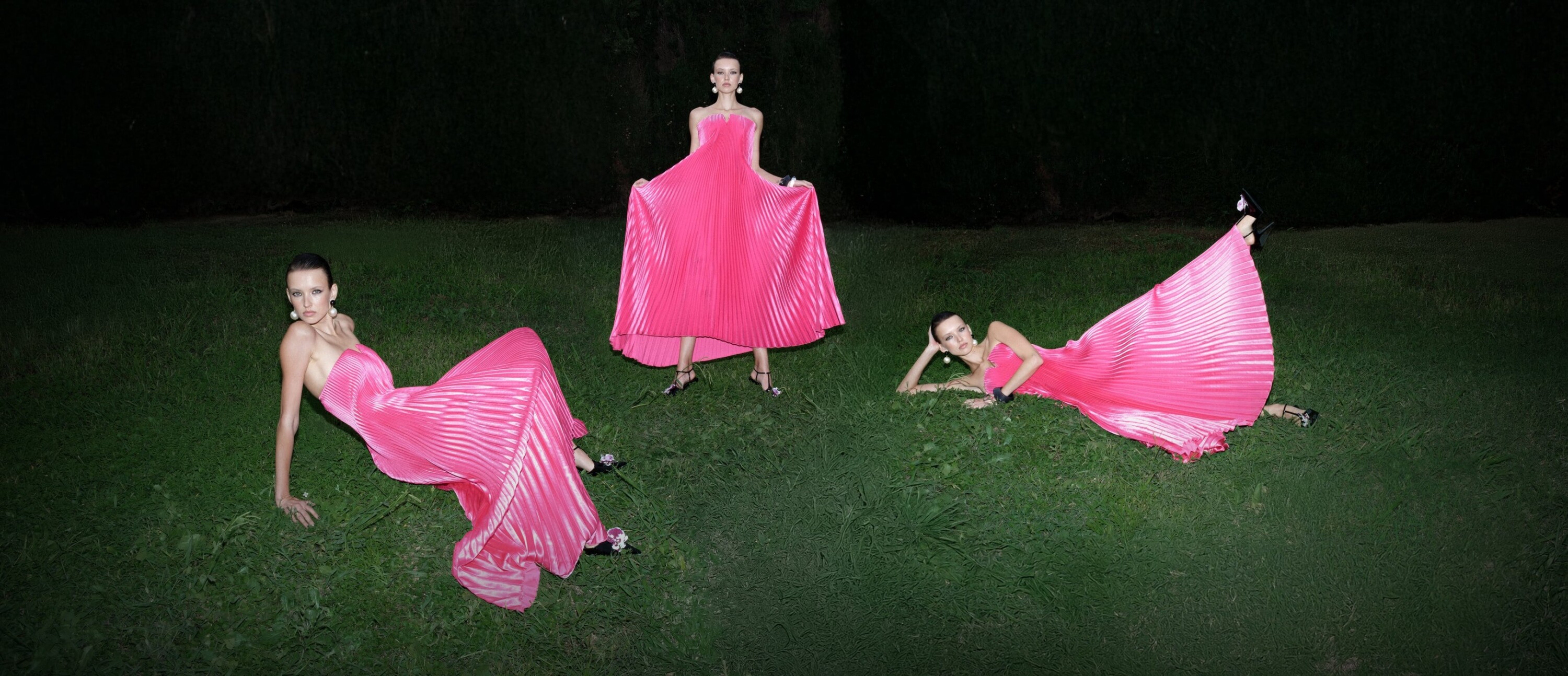 Model in vibrant pink pleated gown posing in three positions on grass at night for L'idee Woman Fall 2024 campaign.