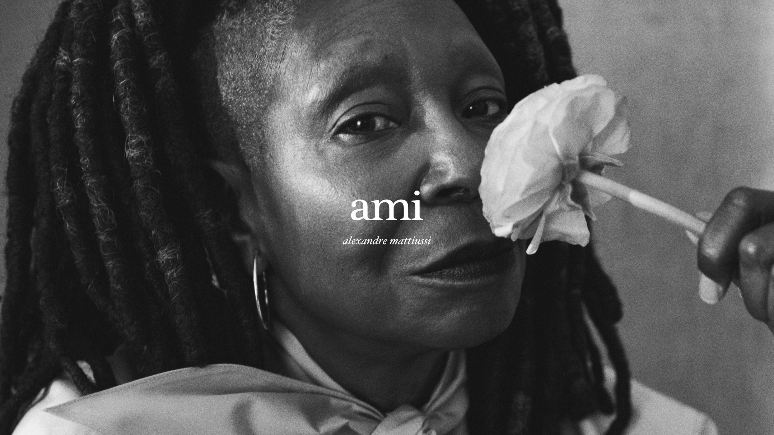 Close-up black and white portrait of Whoopi Goldberg holding a white flower near her face for the Ami Fall 2024 campaign.