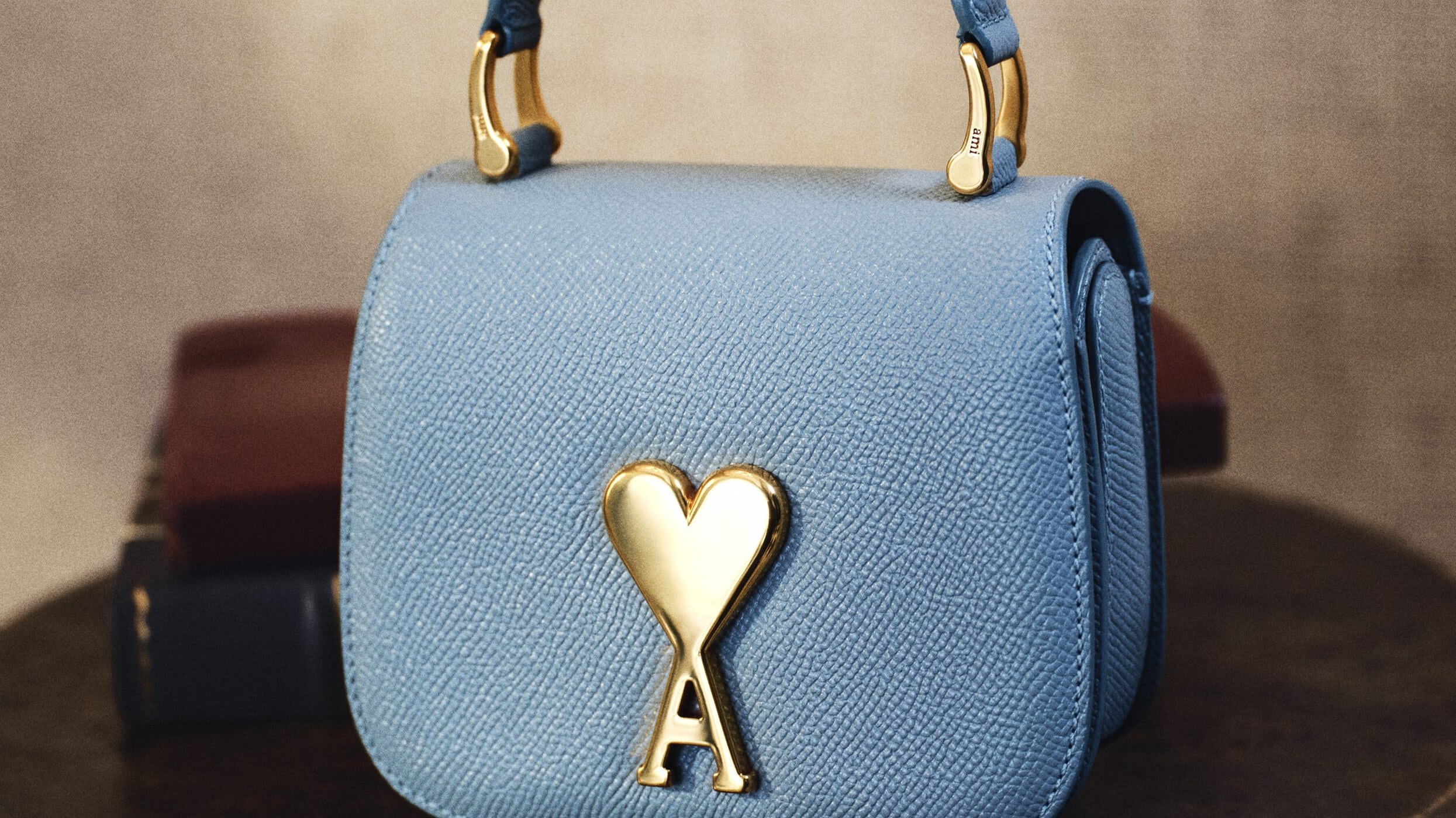 Close-up of a light blue leather handbag with a prominent gold heart logo clasp on a dark surface.