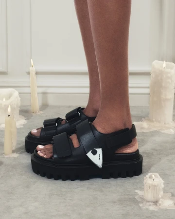 Close-up of legs wearing black chunky sandals with silver hardware surrounded by melting candles.