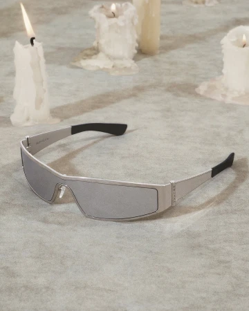 Sleek silver futuristic sunglasses resting on a textured grey surface surrounded by melted white candles.