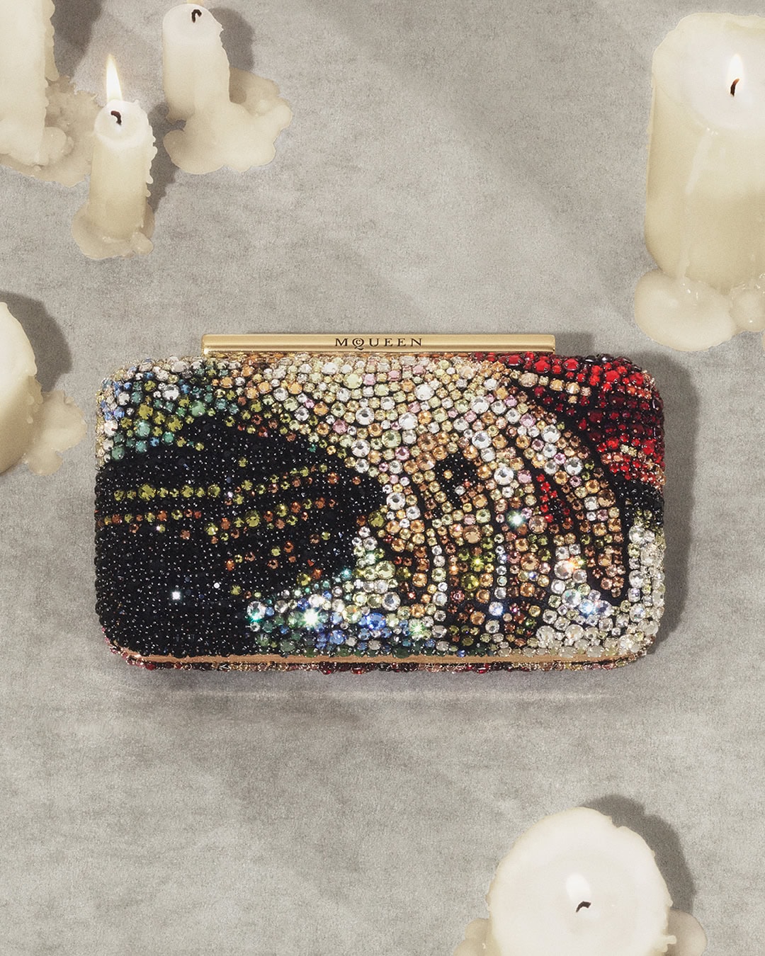 Crystal-embellished McQueen clutch bag surrounded by lit white candles on a textured grey surface