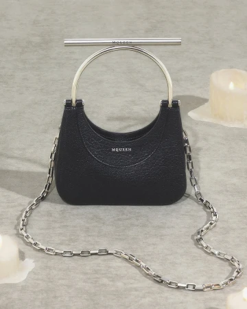 Black textured leather handbag with a silver metal top handle and chain strap on a textured grey surface