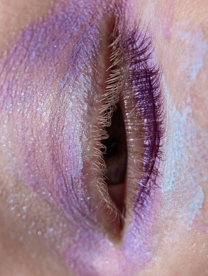Macro shot of a woman's eye with purple and white eyeshadow, visible eyelashes, and brown iris, showcasing beauty and makeup artistry.