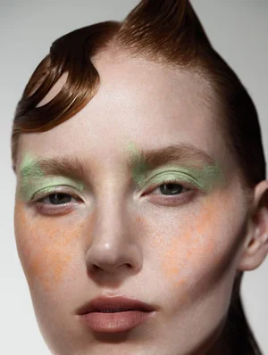 Close up portrait of a female model with sculpted wet look hair, pastel green eyeshadow, and orange blush for Tidal Magazine.