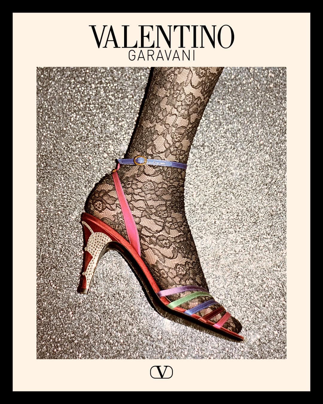 Valentino Garavani shoe campaign image featuring a high-heeled sandal worn with patterned lace tights against a glittering backdrop