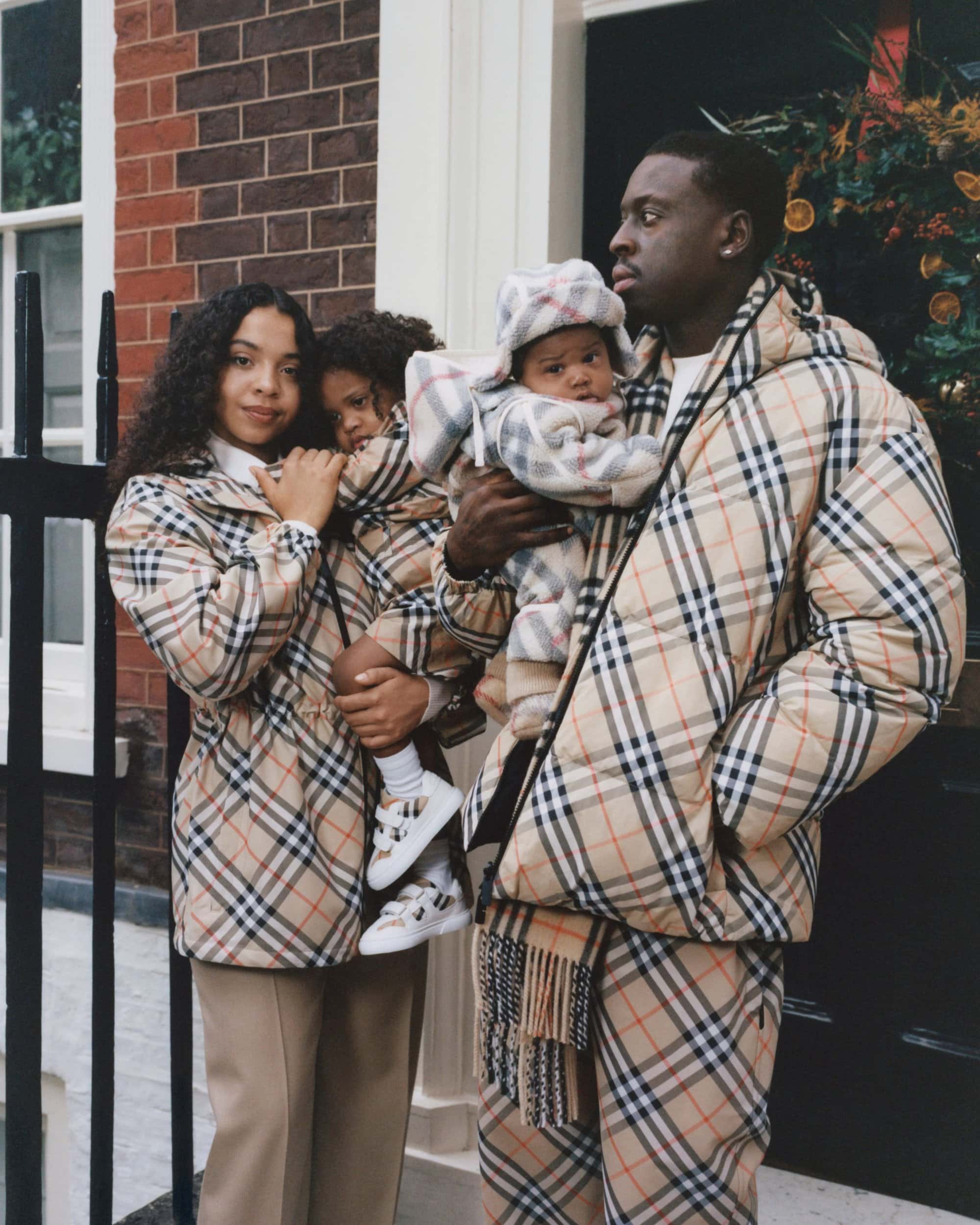 Family wearing matching plaid outerwear standing outside a brick building entrance for the Burberry holiday campaign