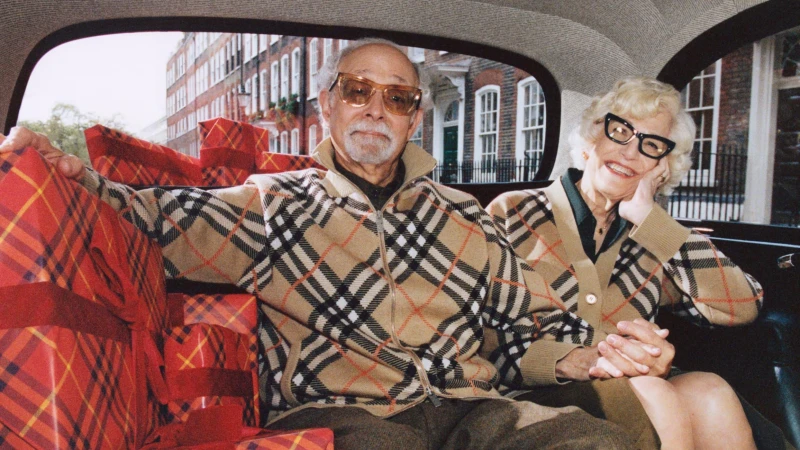 Elderly couple seated inside a vintage car surrounded by red plaid gift boxes for Burberry