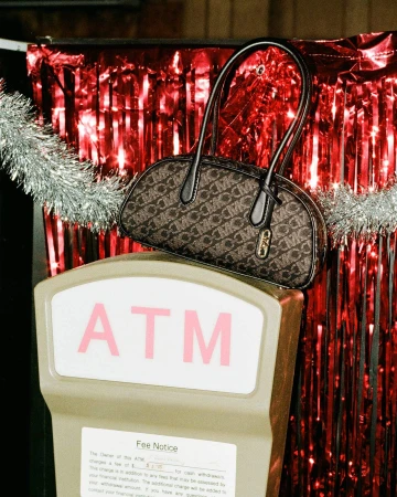 Monogram handbag resting on top of an ATM machine against a red tinsel background with silver garland