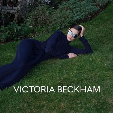 Model in dark sunglasses and long dark dress reclining on a green lawn for Victoria Beckham