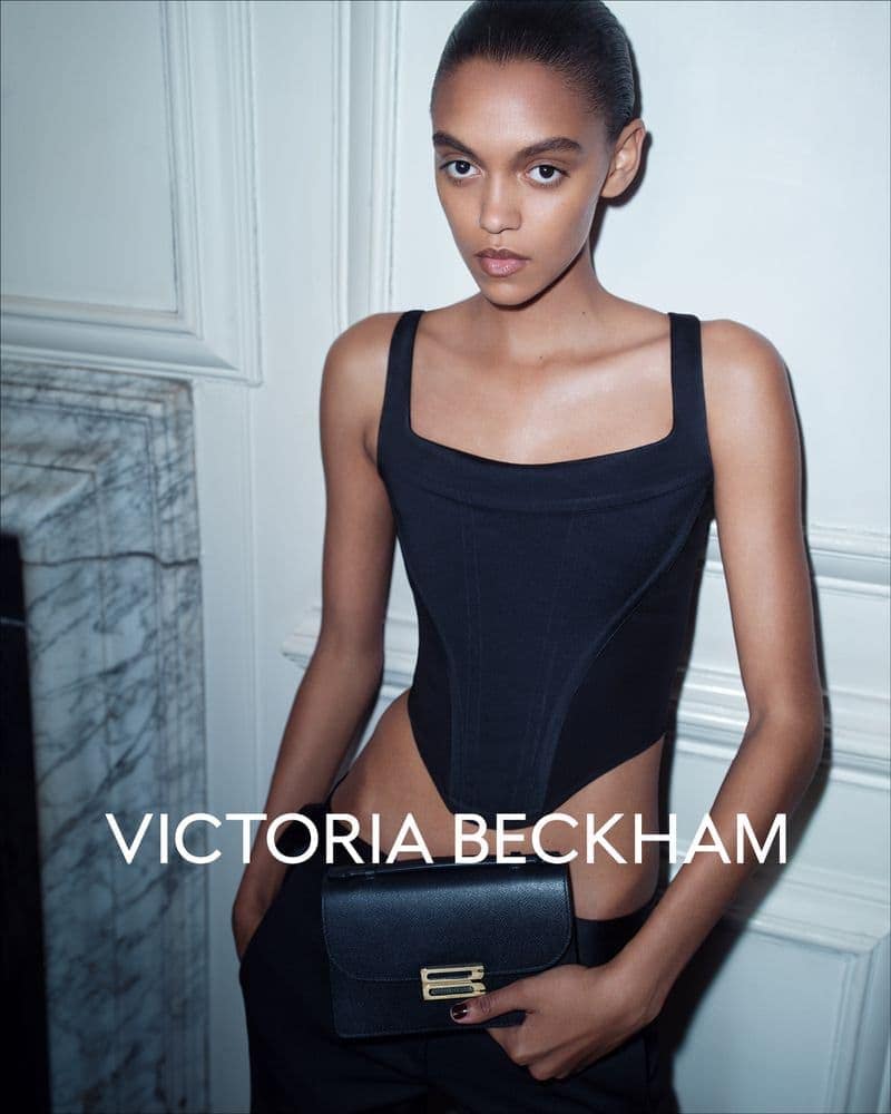Model in a black corset top holding a black handbag against an architectural wall