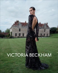 Model in a black sequin gown looking back on a lawn before a historic English country house under an overcast sky.