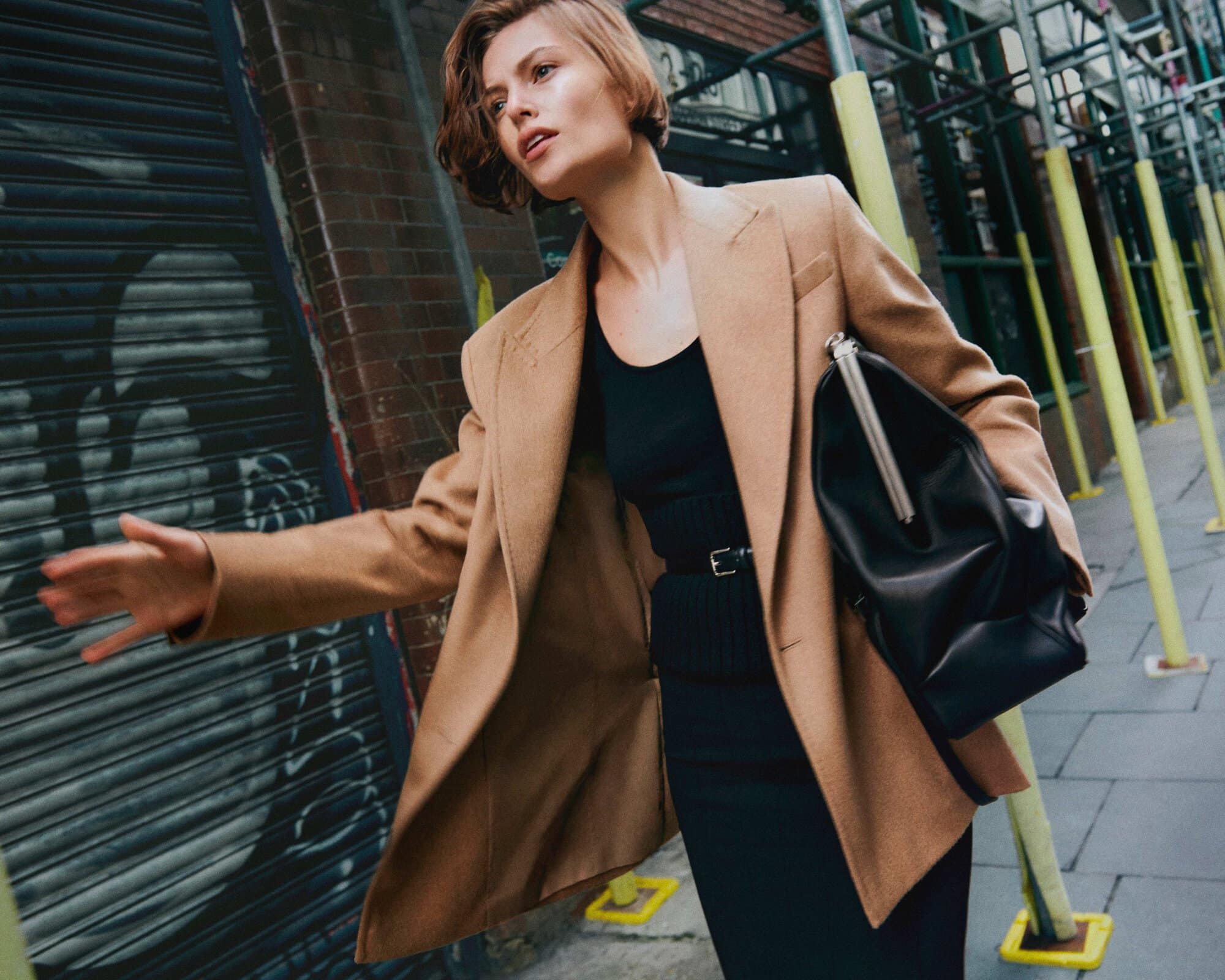 Model wearing a camel blazer and black handbag on a city street for Max Mara Fall 2024 campaign