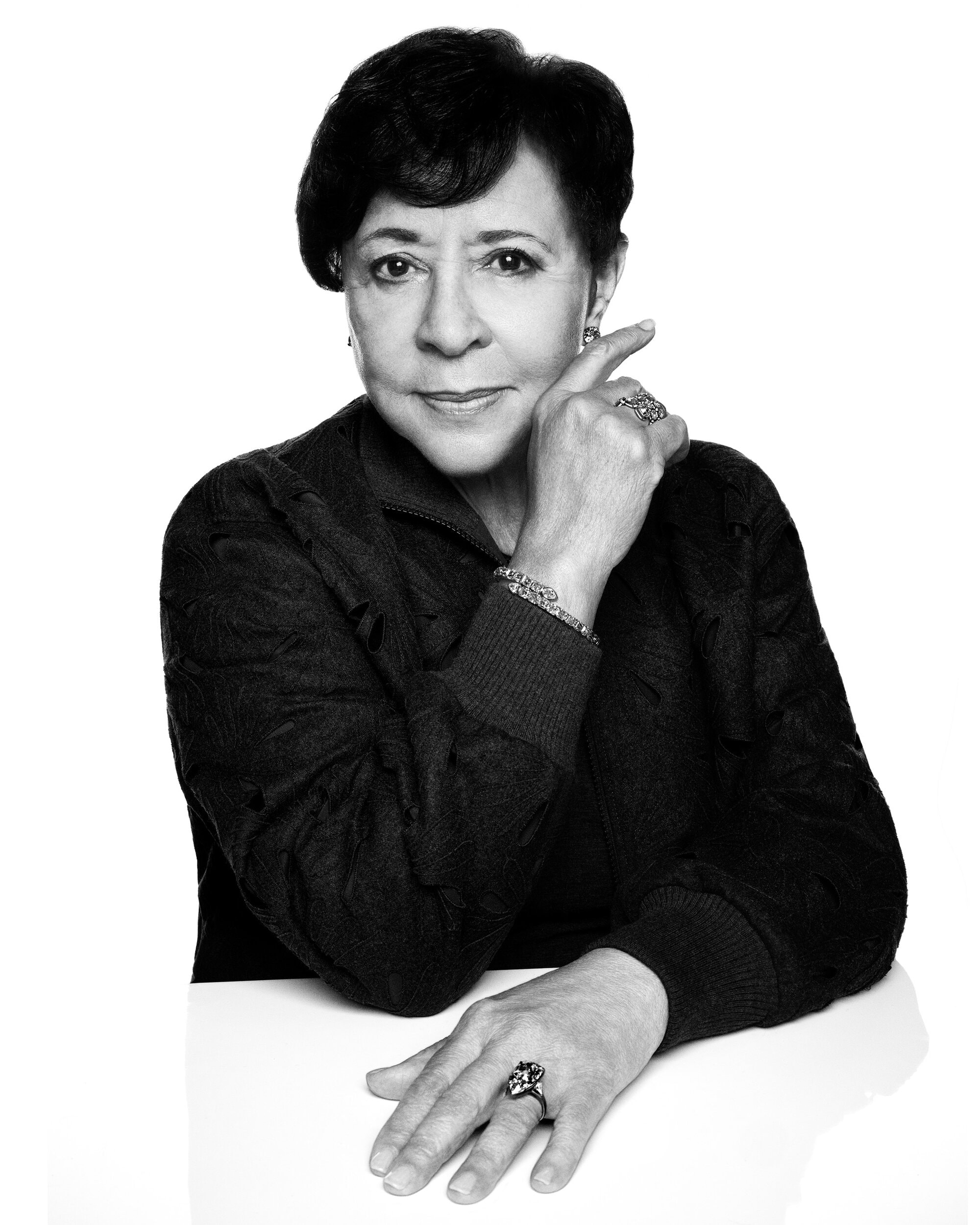 Portrait of Sheila Johnson wearing jewellery and dark patterned jacket against a white seamless background