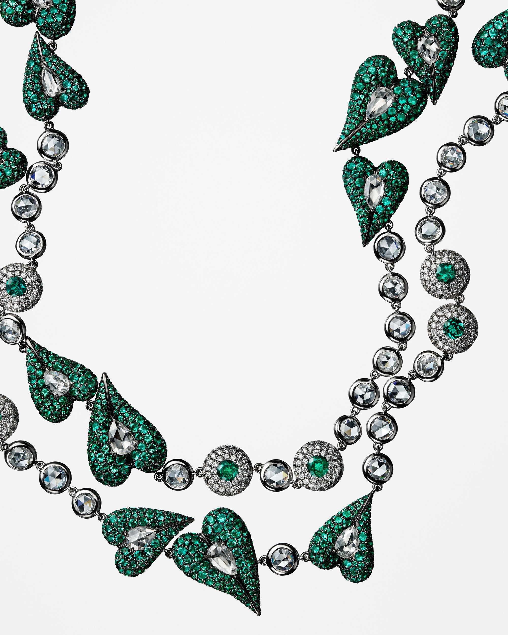 Close-up of diamond and emerald-encrusted heart-shaped necklace by Lugano against a plain white background