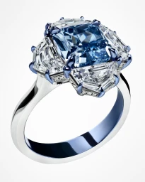 Close-up product shot of a luxury ring featuring a large blue diamond set with white side diamonds on a white background.