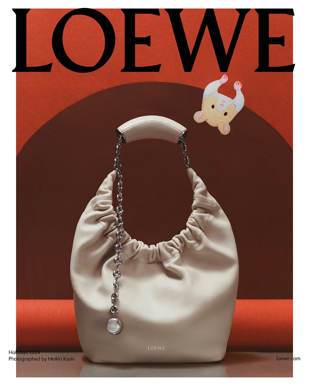 Off-white leather hobo handbag with chain strap displayed against a geometric arch backdrop for Loewe Holiday 2024 campaign