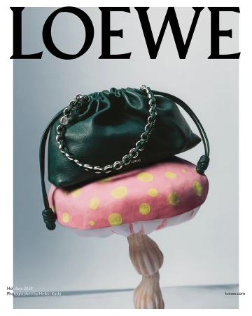 Dark green leather handbag resting on top of a pink polka-dot mushroom sculpture against a light grey studio background.