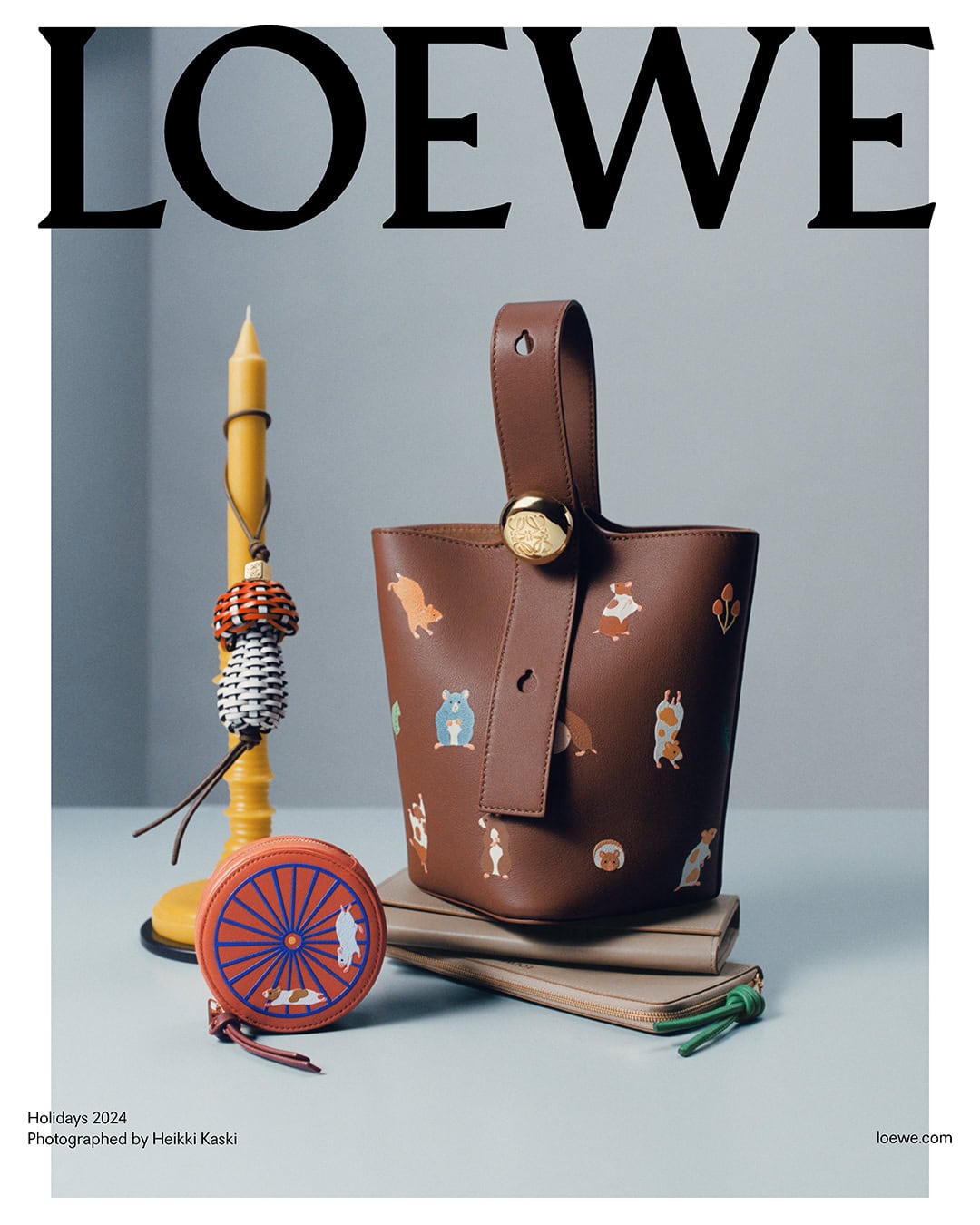 Loewe leather bucket bag featuring whimsical animal illustrations, resting on stacked notebooks with a yellow candle and round coin purse.