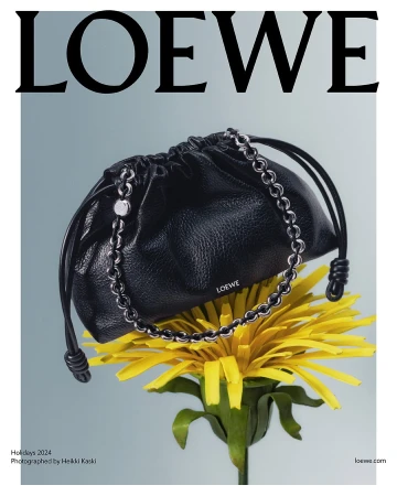 Black leather Loewe handbag resting on a bright yellow dandelion flower against a pale grey background