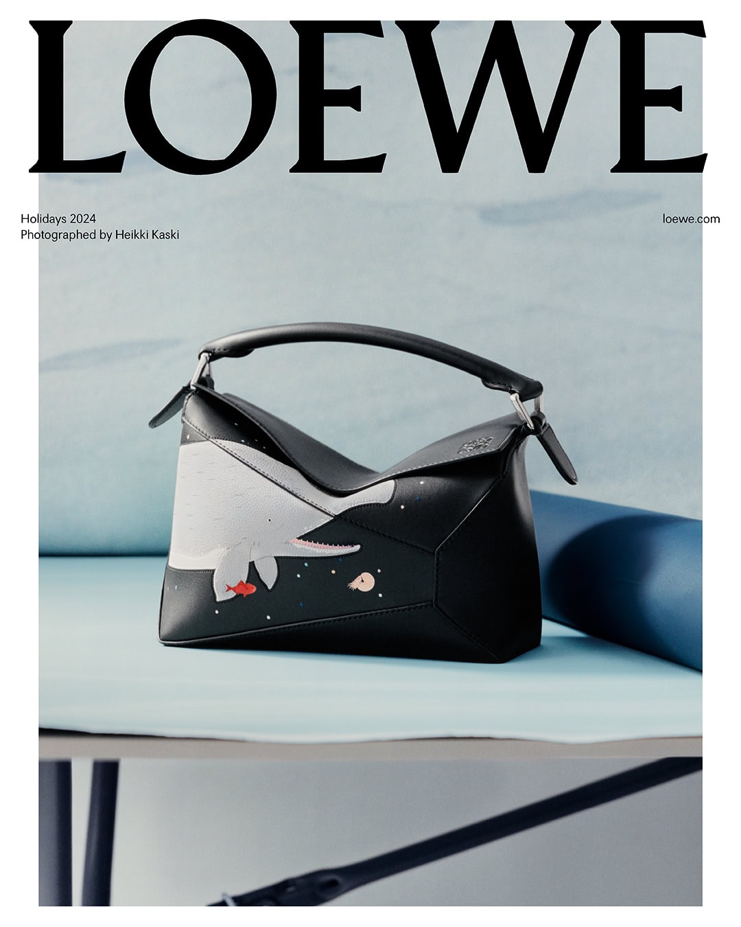 Loewe black leather puzzle bag featuring white graphic whale design resting on pale blue studio surface