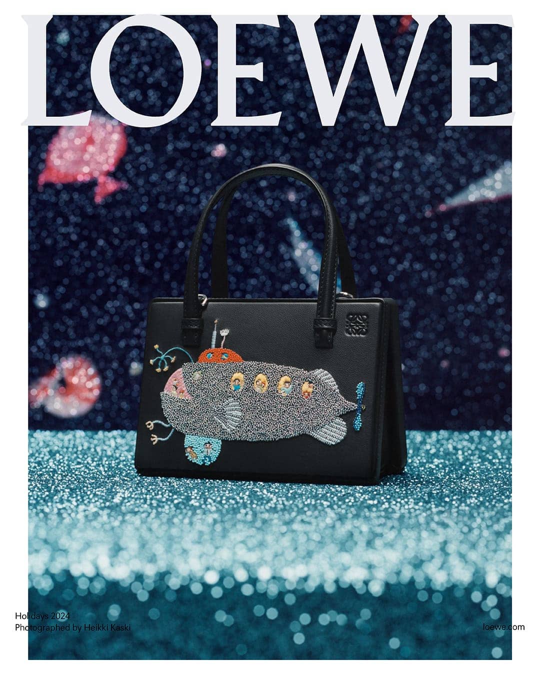 Black leather handbag with embroidered submarine design resting on a sparkling turquoise textured surface against a dark starry background