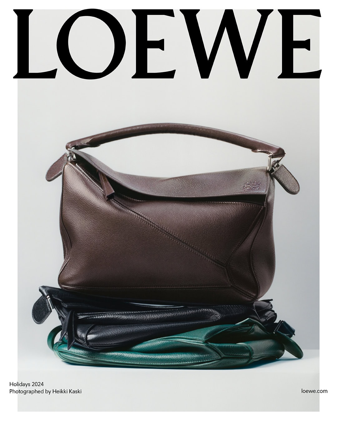 Stacked leather handbags featuring a large brown structured bag resting on black and green bags against white