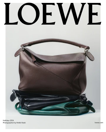 Stacked leather handbags featuring a large brown structured bag resting on black and green bags against white