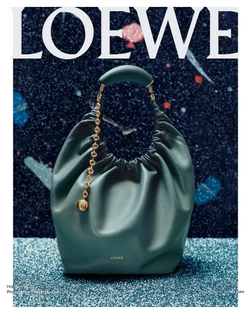 Green leather shoulder bag with a gold chain strap resting on a sparkly blue surface against a dark cosmic background