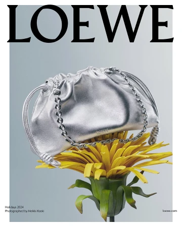 Silver metallic handbag resting on a large yellow flower against a gradient grey background
