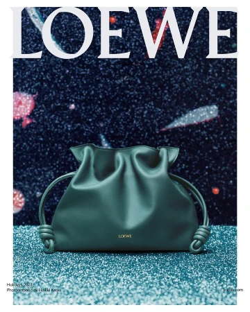 Green leather Loewe handbag resting on a sparkling teal glitter surface against a cosmic background