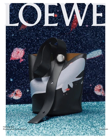 Black leather bucket bag with whale illustration on a glittering blue surface against a dark starry background