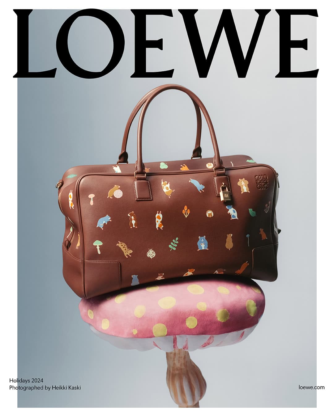 Brown leather handbag with animal illustrations resting on a pink mushroom prop against a light gradient background