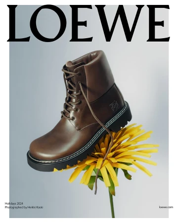 Brown leather boot resting on top of a bright yellow dandelion flower against a pale gradient background