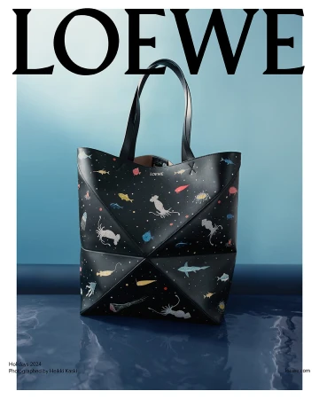 Black leather tote bag with colorful marine life illustrations set against a blue gradient studio backdrop with water reflection.