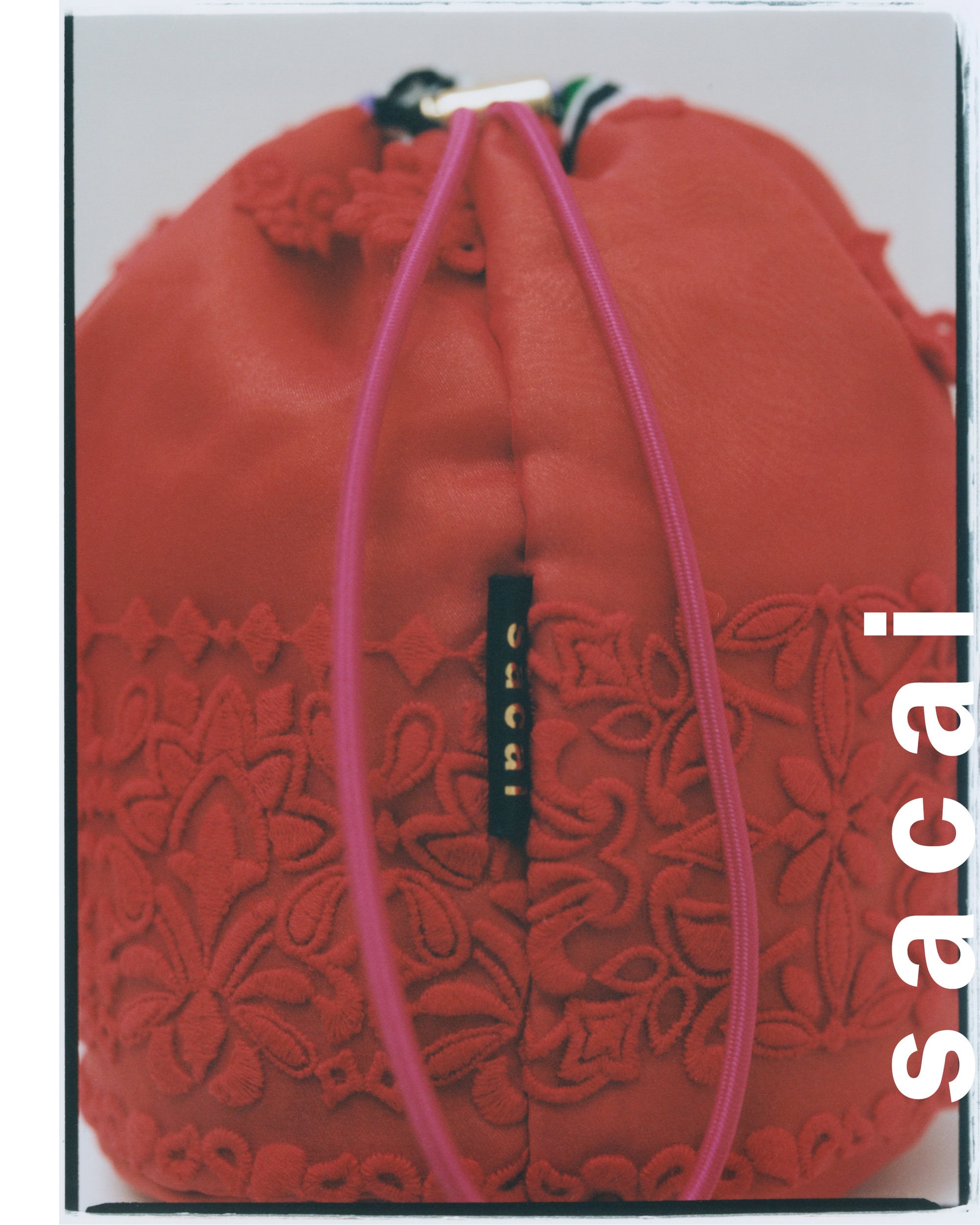 Close up of a red drawstring bucket bag with ornate embroidered patterns against a neutral studio background