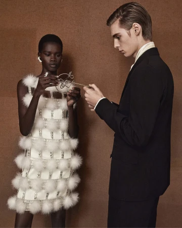 A woman wearing a textured white feather-trimmed dress stands next to a man in a dark suit holding a metallic accessory.