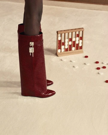Close-up of tall red snakeskin boots with silver padlock hardware on a pale carpet near a wooden game set