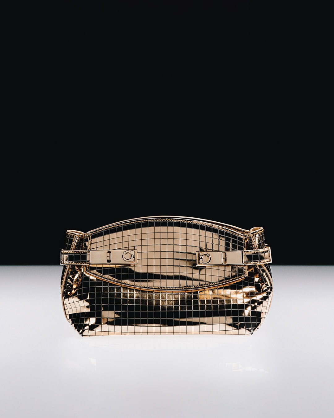 Metallic gold grid handbag resting on a reflective white surface against a contrasting black background.