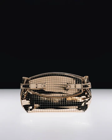 Metallic gold grid handbag resting on a reflective white surface against a contrasting black background.