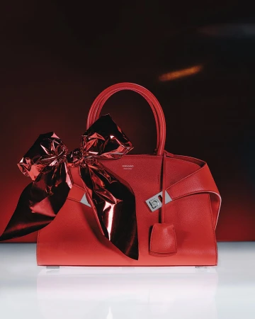 Red leather handbag adorned with a large metallic red foil bow against a dark red and white gradient background
