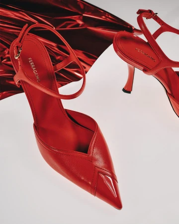 Two red leather high-heeled slingback shoes against a white backdrop with a metallic red foil prop.