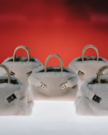 Five plush white faux-fur handbags with patent handles arranged against a vibrant red background.