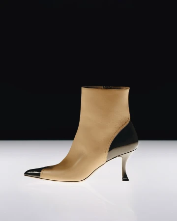 Tan leather ankle boot with black patent toe and heel cap on a reflective white surface against a dark background