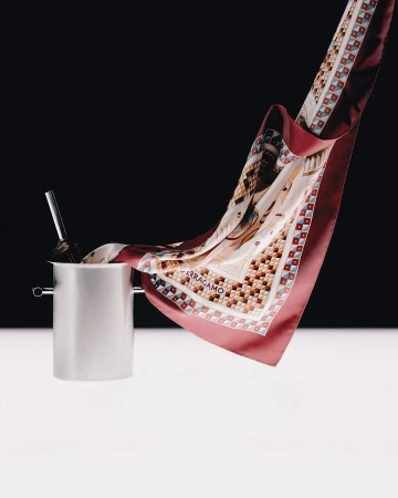Silk scarf floating out of a metal ice bucket against a two-tone black and white studio background