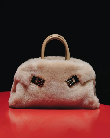 Cream shearling handbag with leather top handles resting on a glossy red surface against a solid black background.
