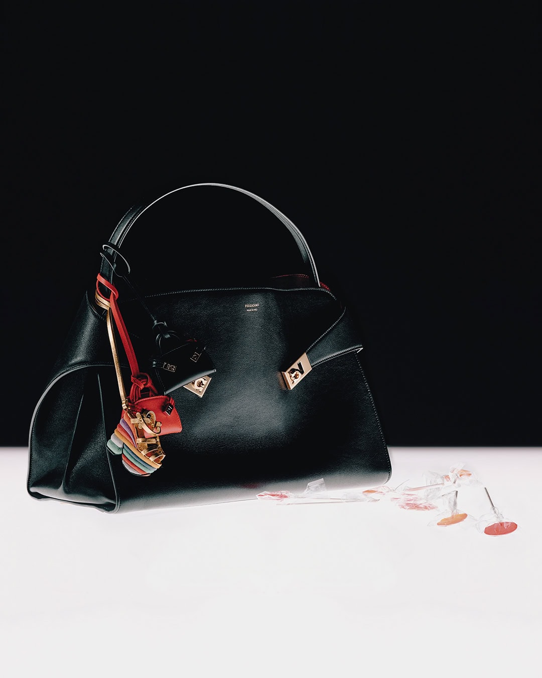 Black leather handbag with decorative charms resting on a white surface against a contrasting black background for Ferragamo